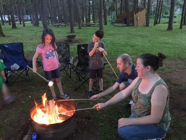 A group of people sitting around a campfire at an RV campground.