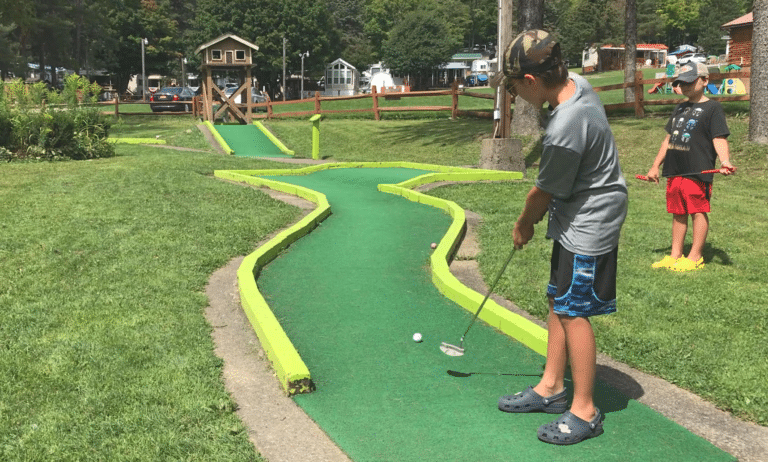 A boy is playing miniature golf in a park located in Western New York.