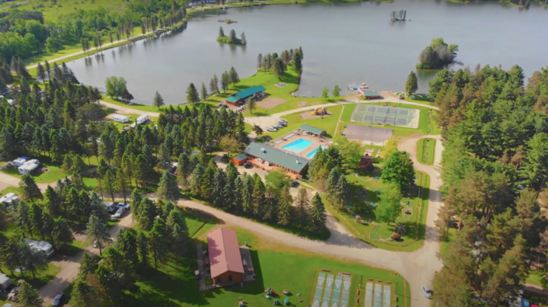 An aerial view of a campground and lake, surrounded by families enjoying their time camping and staying in cabins.