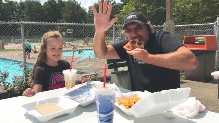 A family enjoying pizza at a poolside cabin in a campground.