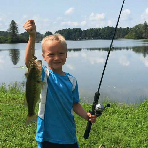 A young boy holding up a fish in front of Rainbow Lake.