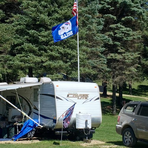 A cabin-like RV parked in a grassy area with a flag at a campground in WNY.